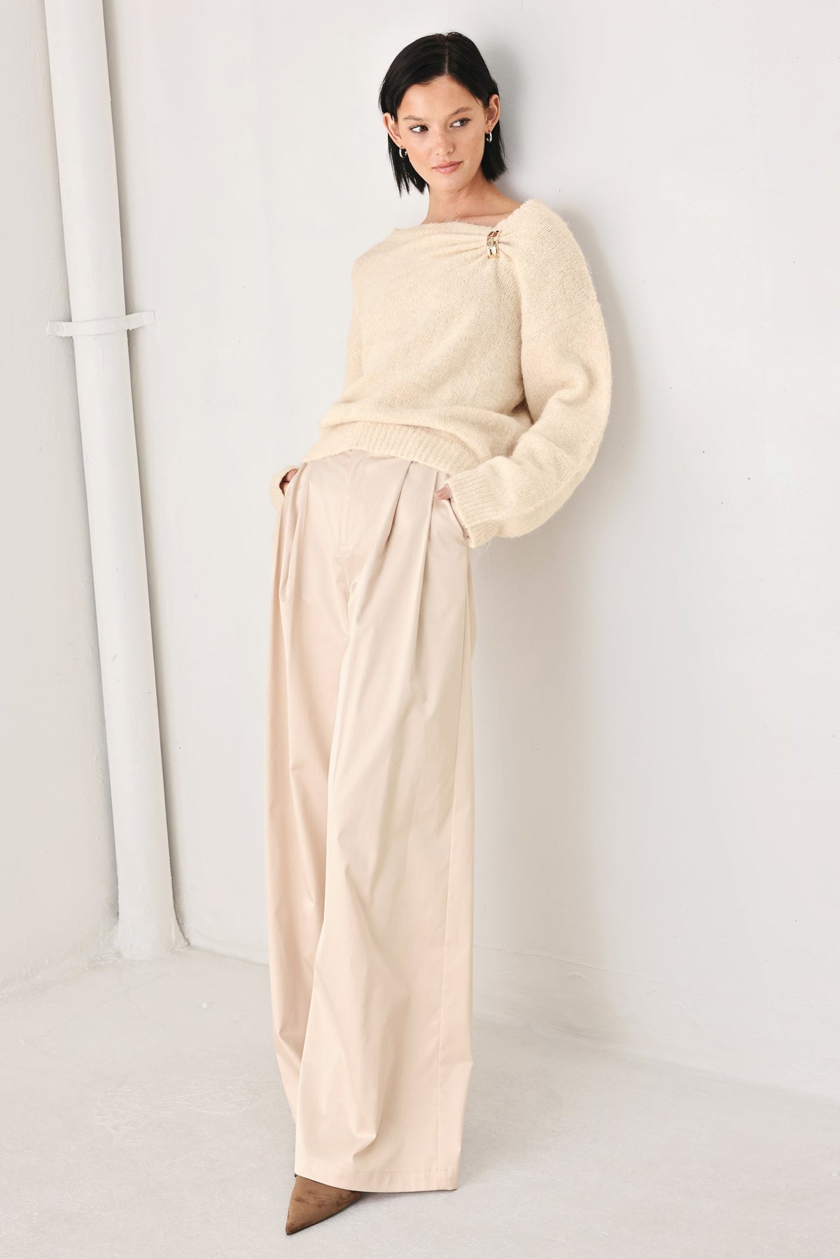 Ivory cinched-neck sweater with long sleeves and gold charm detail at collar
