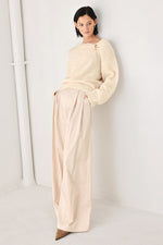 Ivory cinched-neck sweater with long sleeves and gold charm detail at collar
