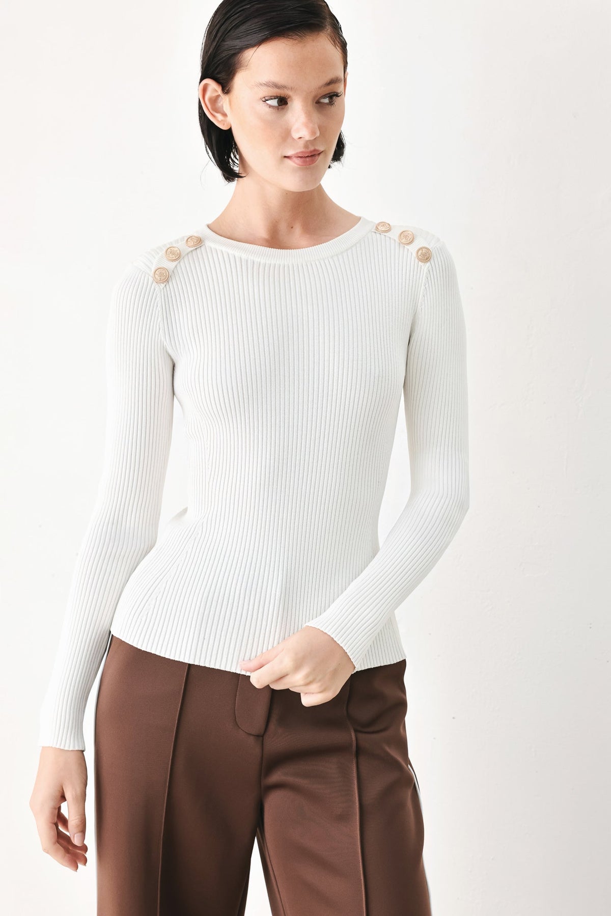 Off-white ribbed sweater top with crew neck, long sleeves, and gold button accents on shoulders