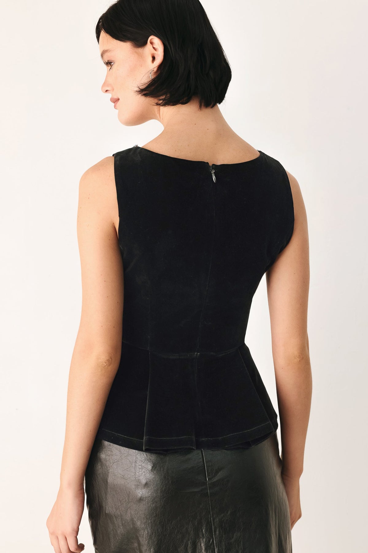 Back view of black sleeveless velvet peplum top with central seam