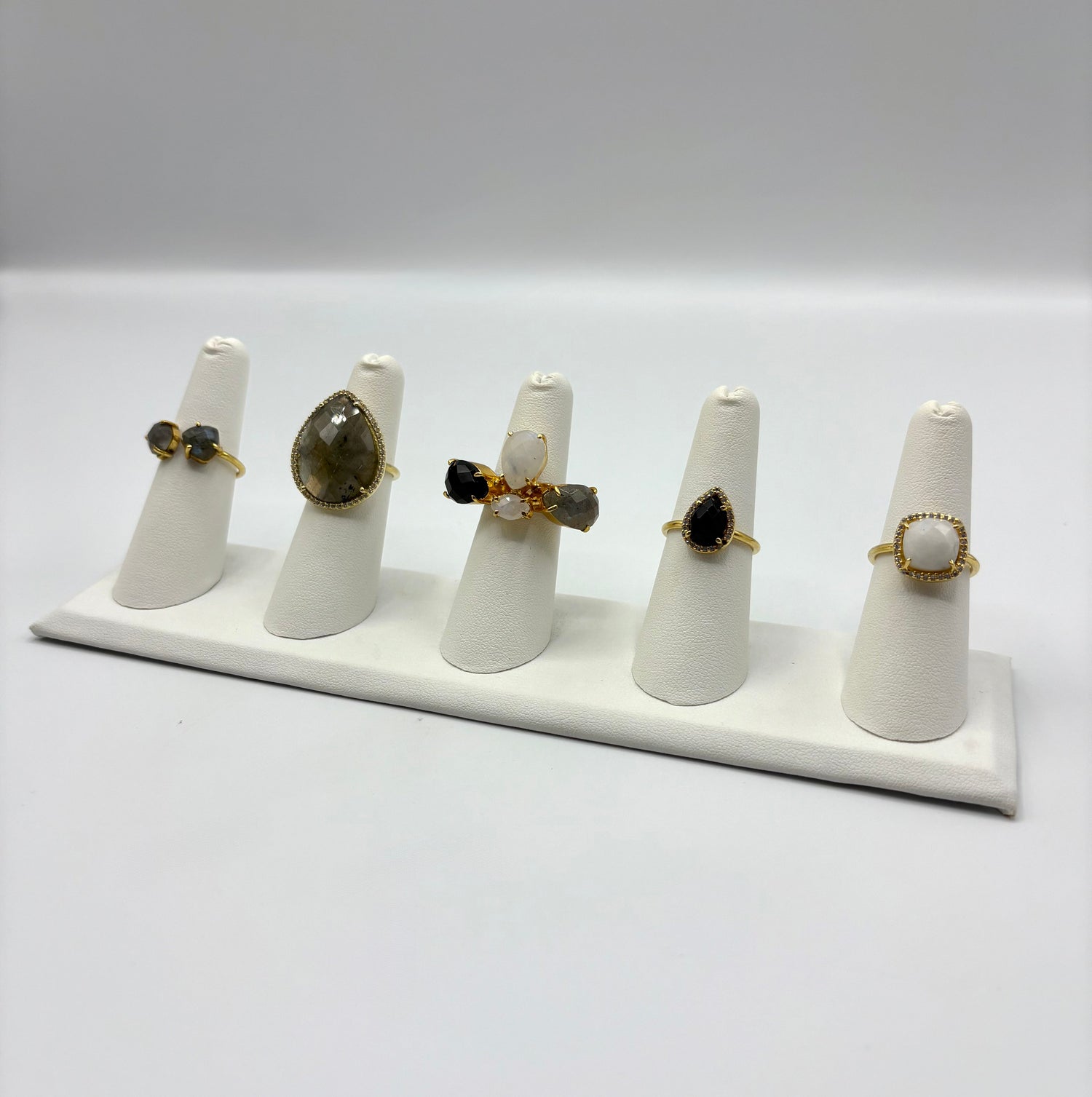 Gold-tone gemstone rings on white display stands with opal, smoky gray, and black stones
