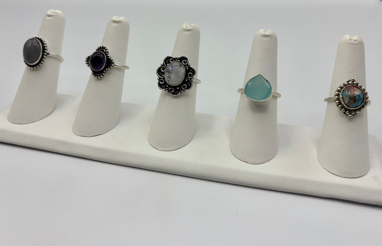 Five silver-tone rings with black, purple, and teal cabochon stones on display stands