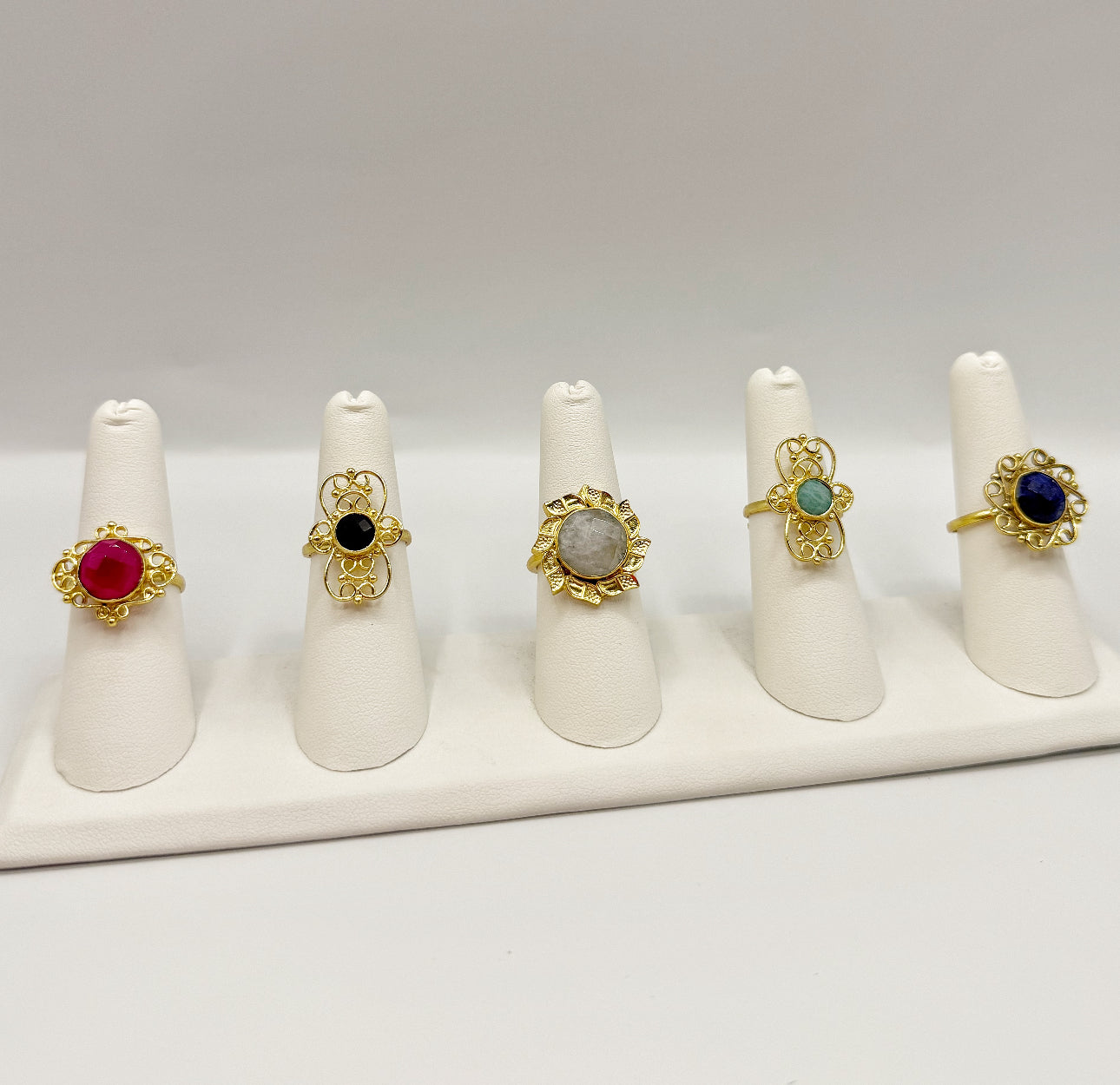 Gold ring set on white stands, featuring red, turquoise, and dark blue gemstones