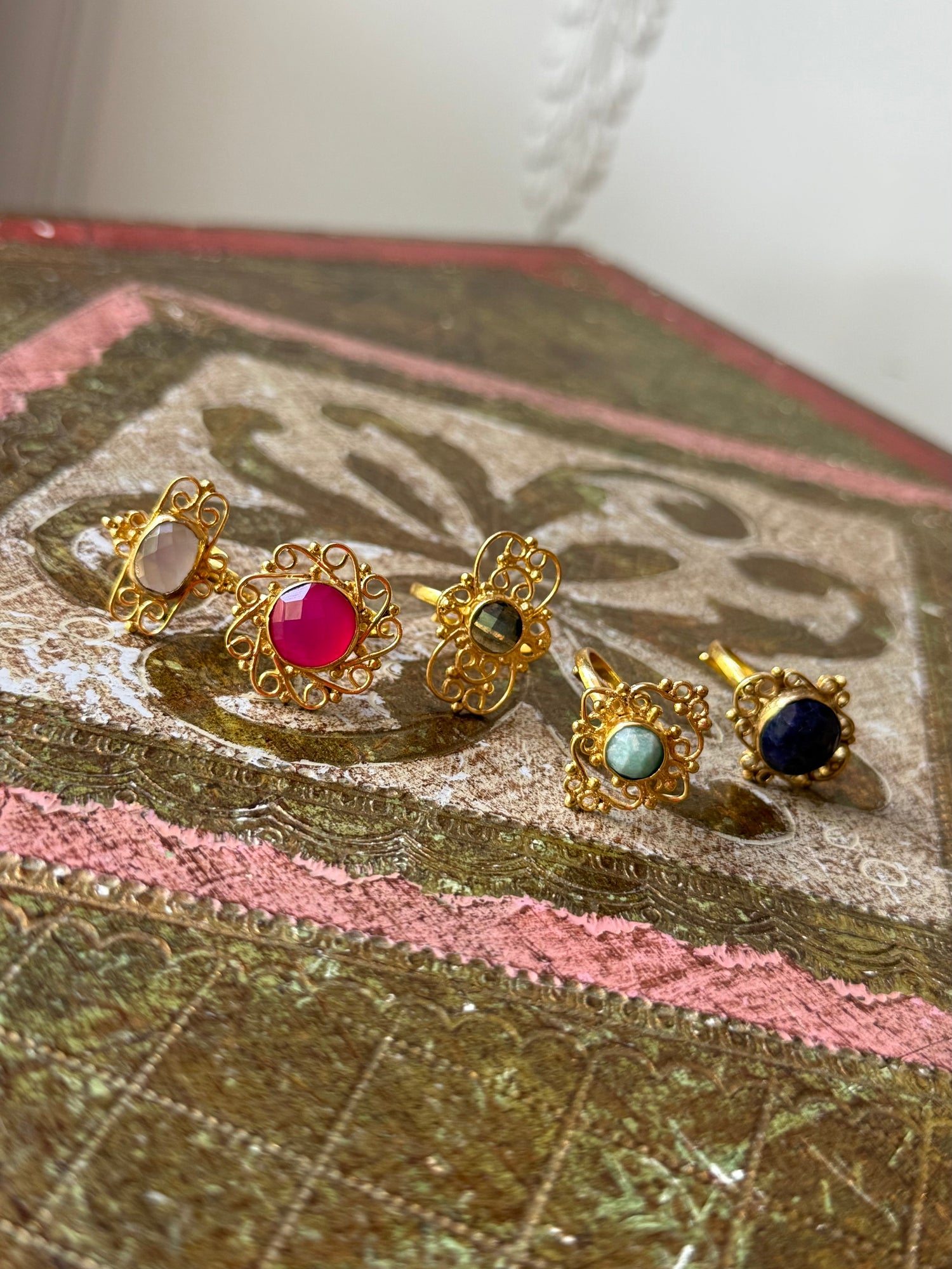Gold gemstone ring set with red, green, and dark blue stones, close-up on fabric