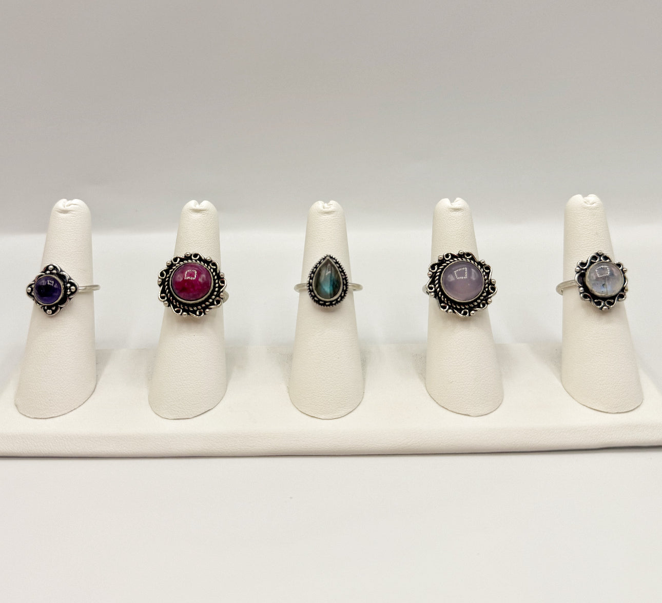Five assorted gemstone rings displayed on white ring stands
