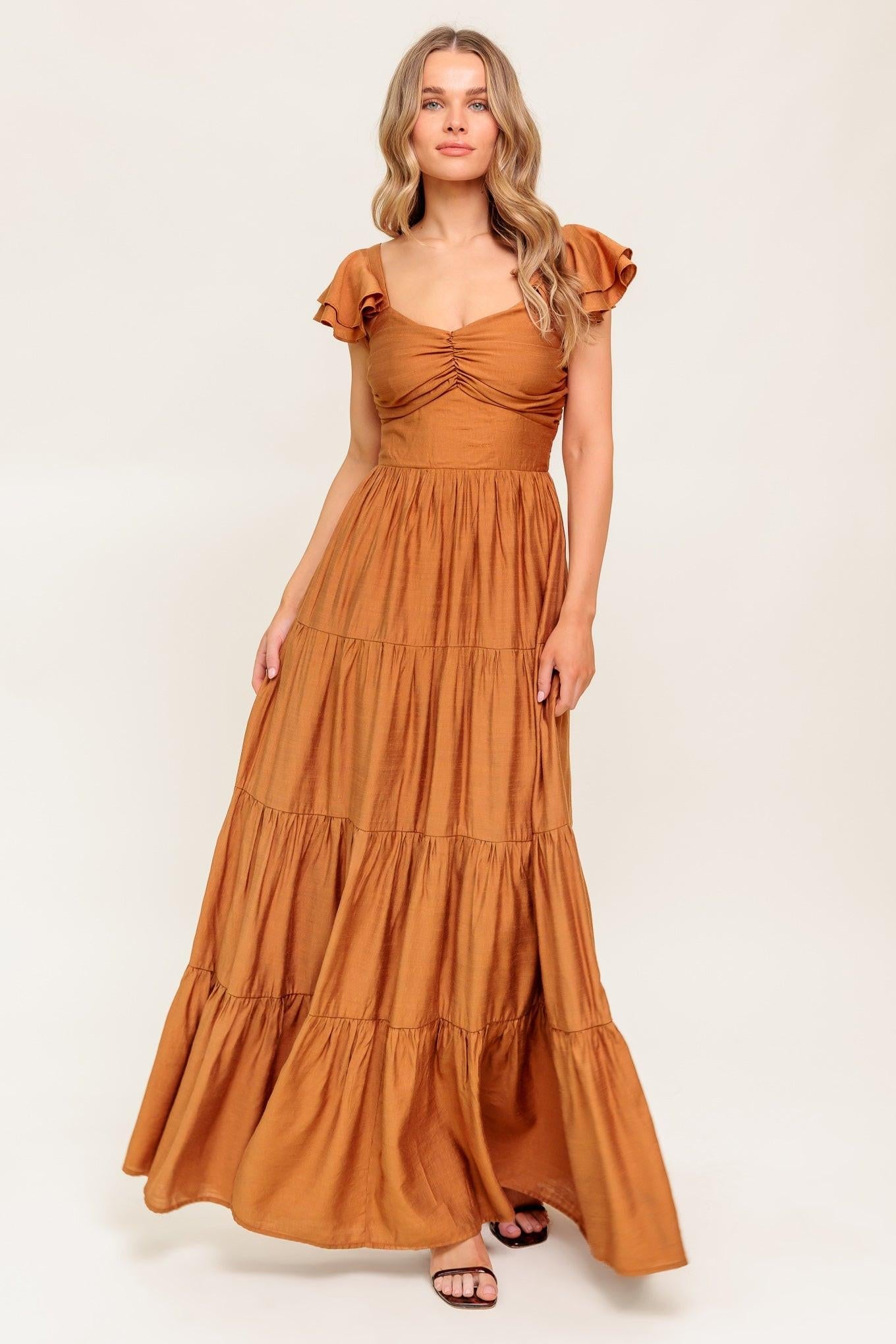 Rust woven maxi dress with ruched bust, tiered skirt, and ruffle cap sleeves.