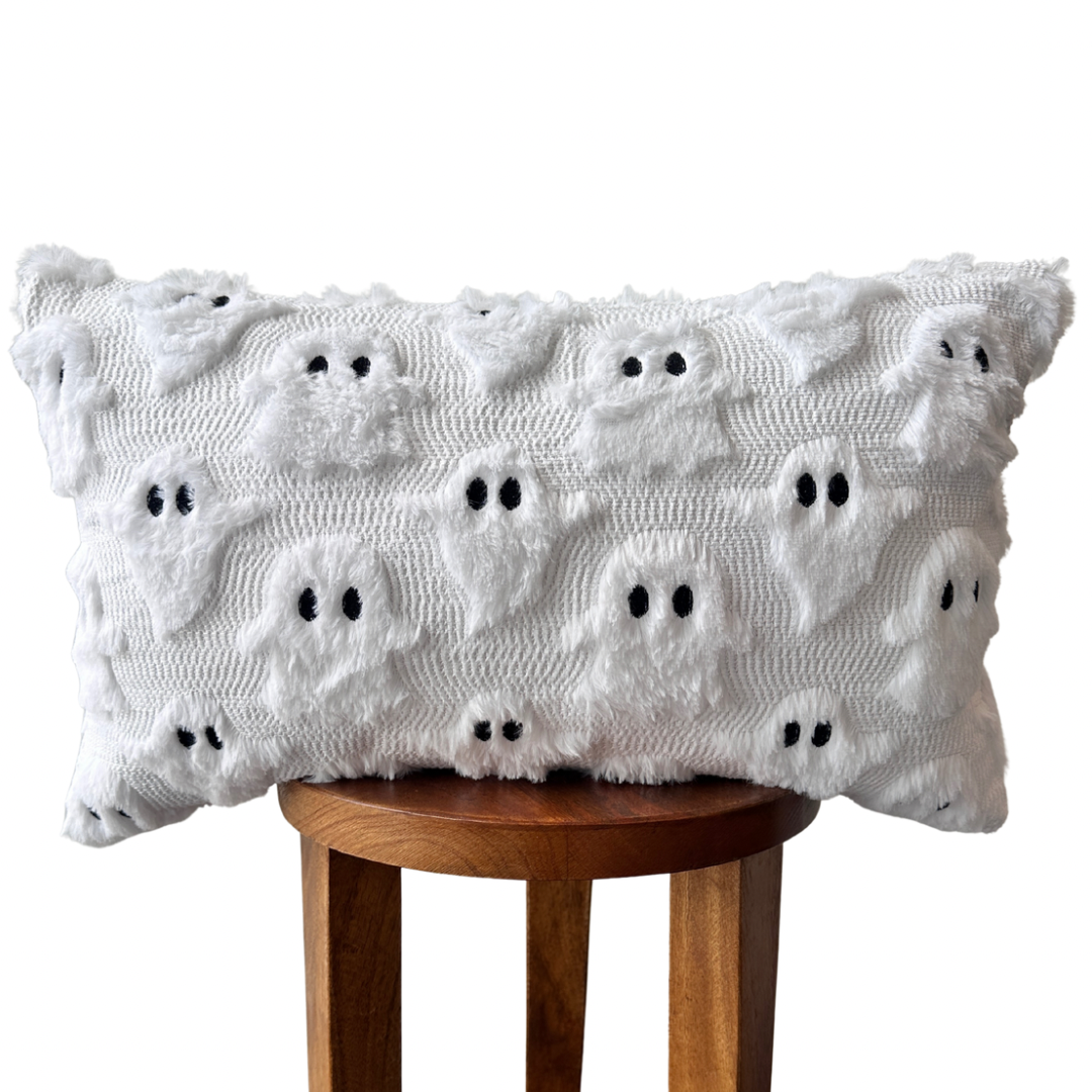 White textured lumbar pillow cover with raised ghost faces and embroidered black eyes