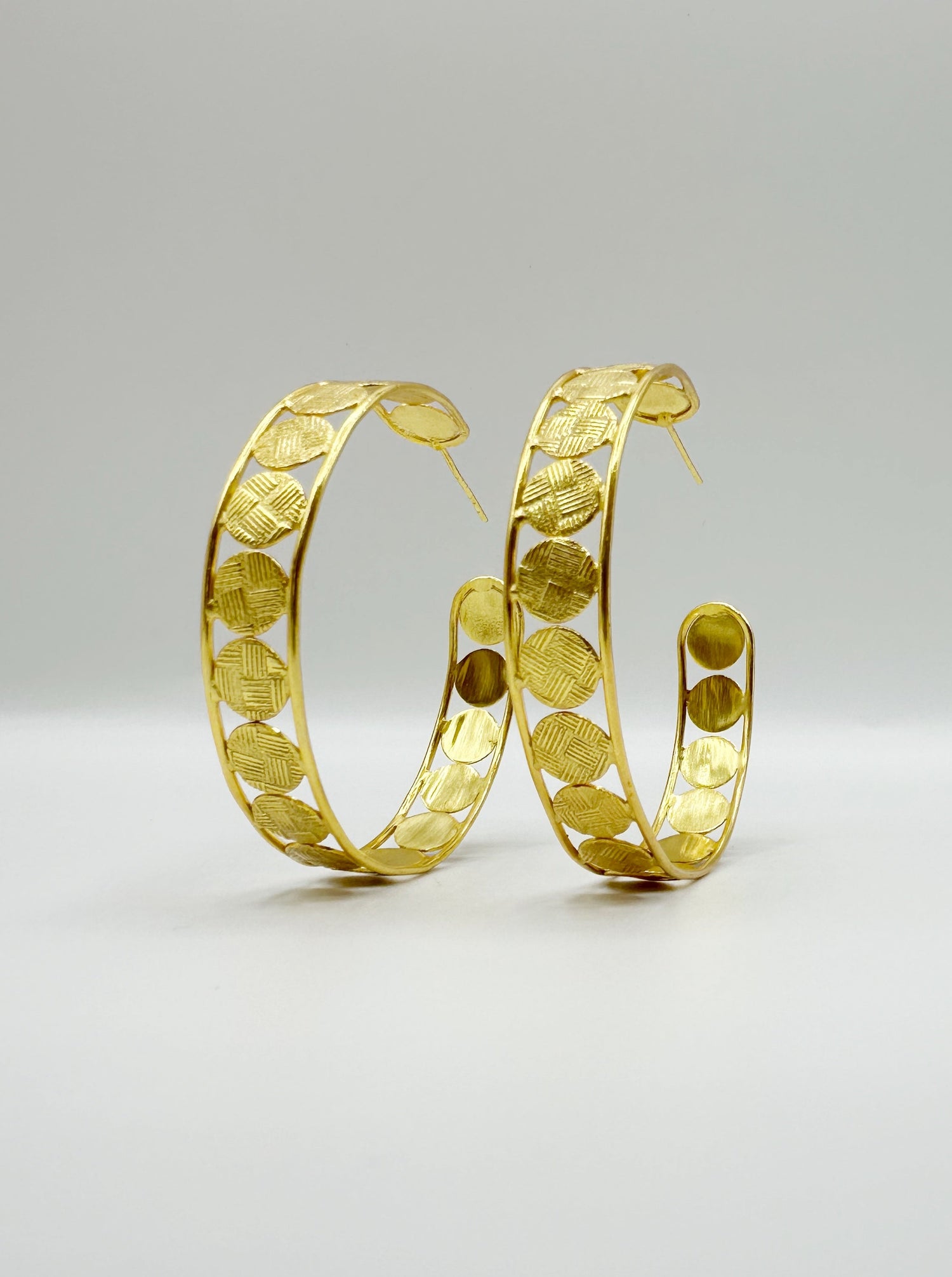 Large gold hoop earrings with textured geometric pattern, studio pair view