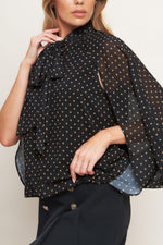 Black woven top with gold dot print, draped tie neck and flowy sleeves