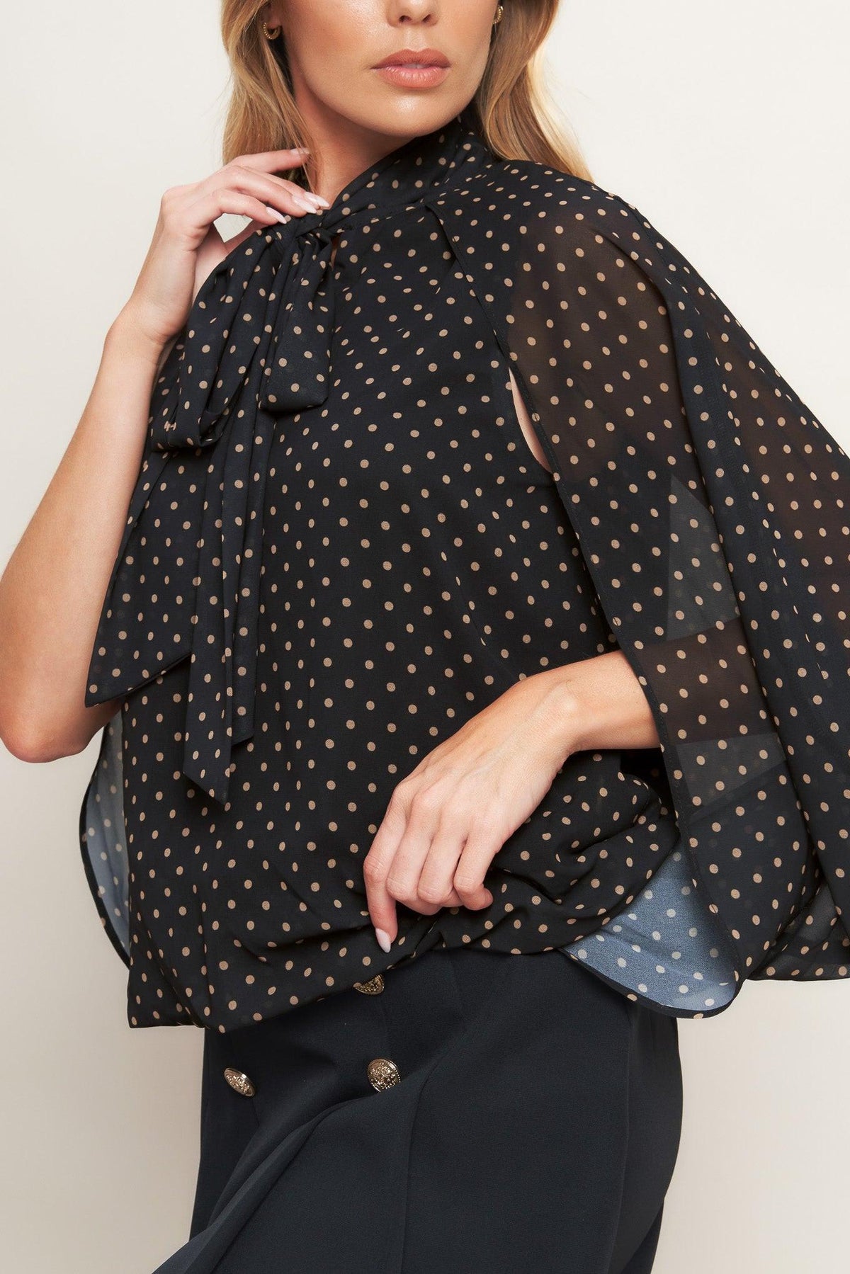 Black woven top with gold dot print, draped tie neck and flowy sleeves