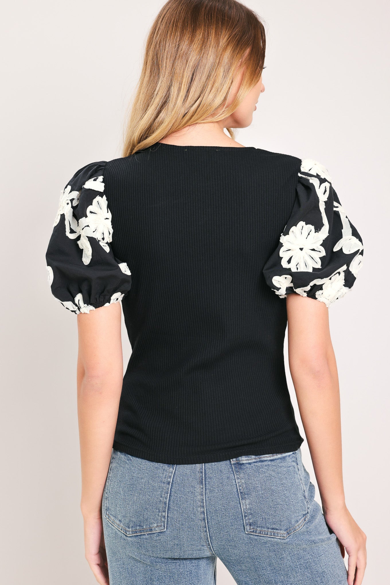 Black ribbed knit V-neck top with puff sleeves and white floral back detail