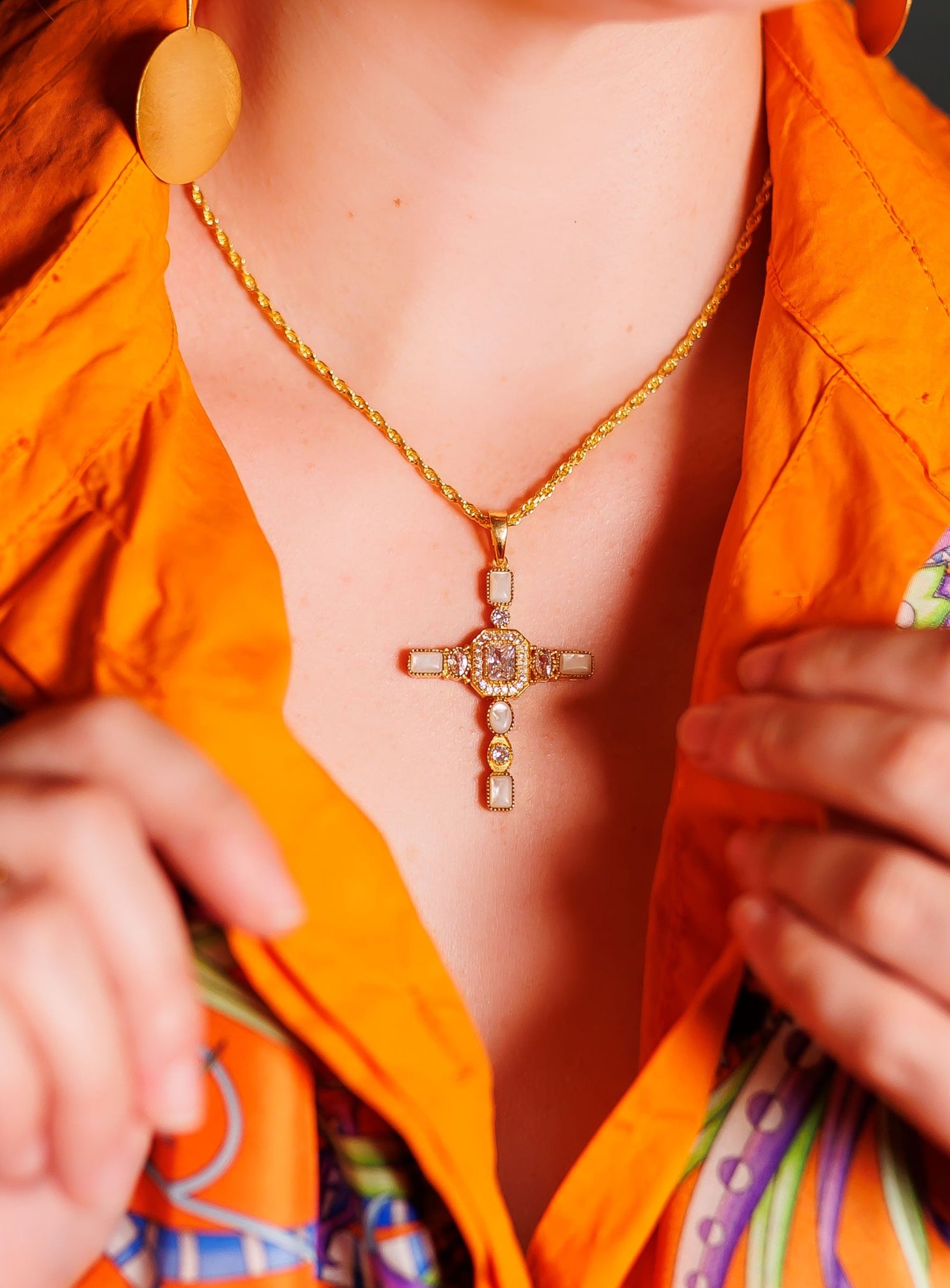 Gold cross pendant necklace with multicolor stones, layered chain, close-up
