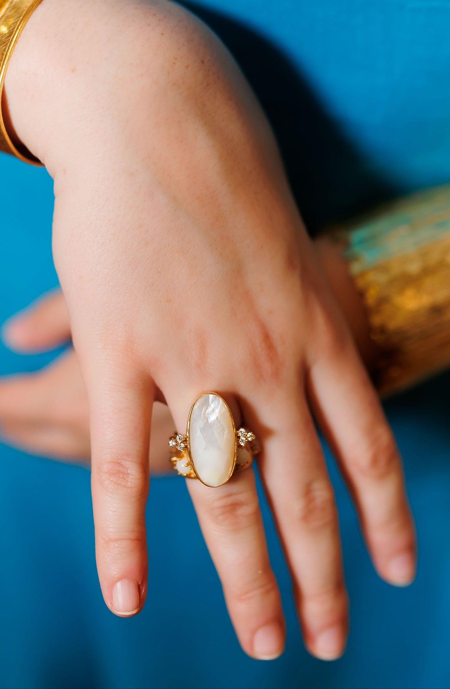Gold-tone oval mother-of-pearl ring with small crystal accents, worn on hand