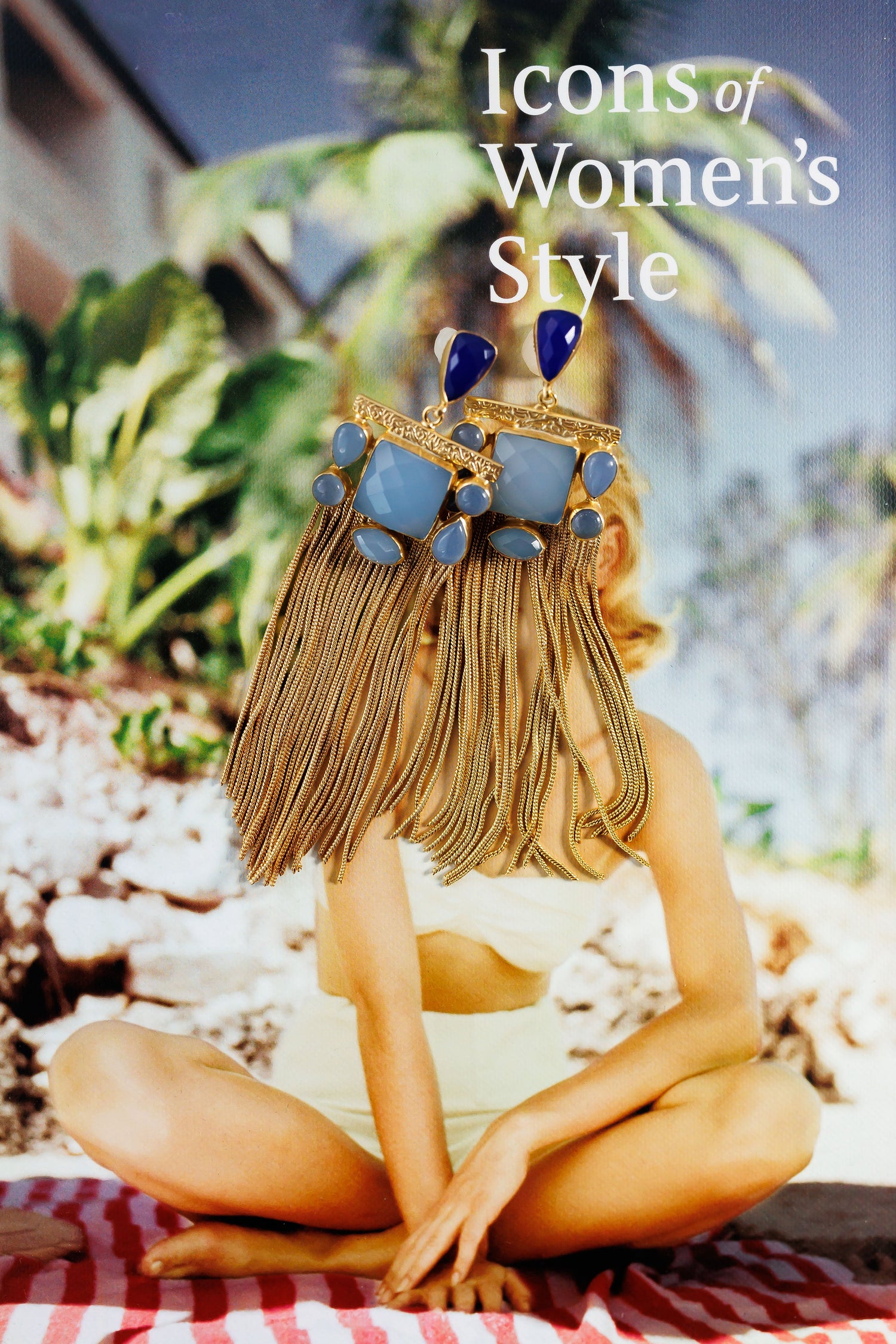 Gold tassel earrings with blue stones and geometric studs, seated view.
