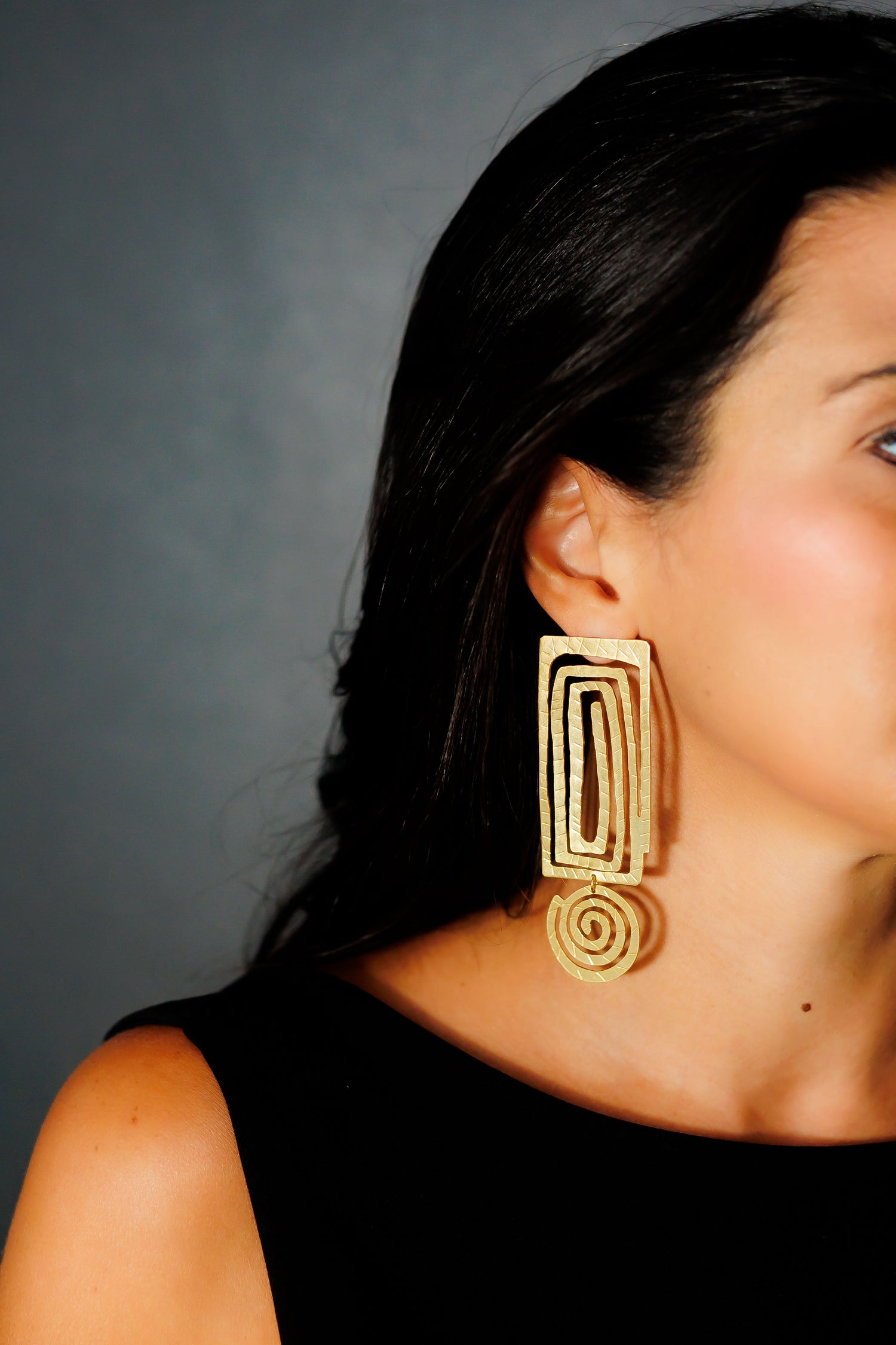 Geometric gold statement drop earrings with rectangular and spiral shapes, worn with black top