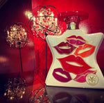 White perfume bottle with red cap, colorful lips graphic and gold NYC seal