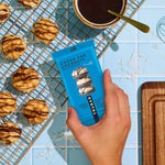 TruBar cocoa for coconuts protein bar held in hand beside cookies on wire rack