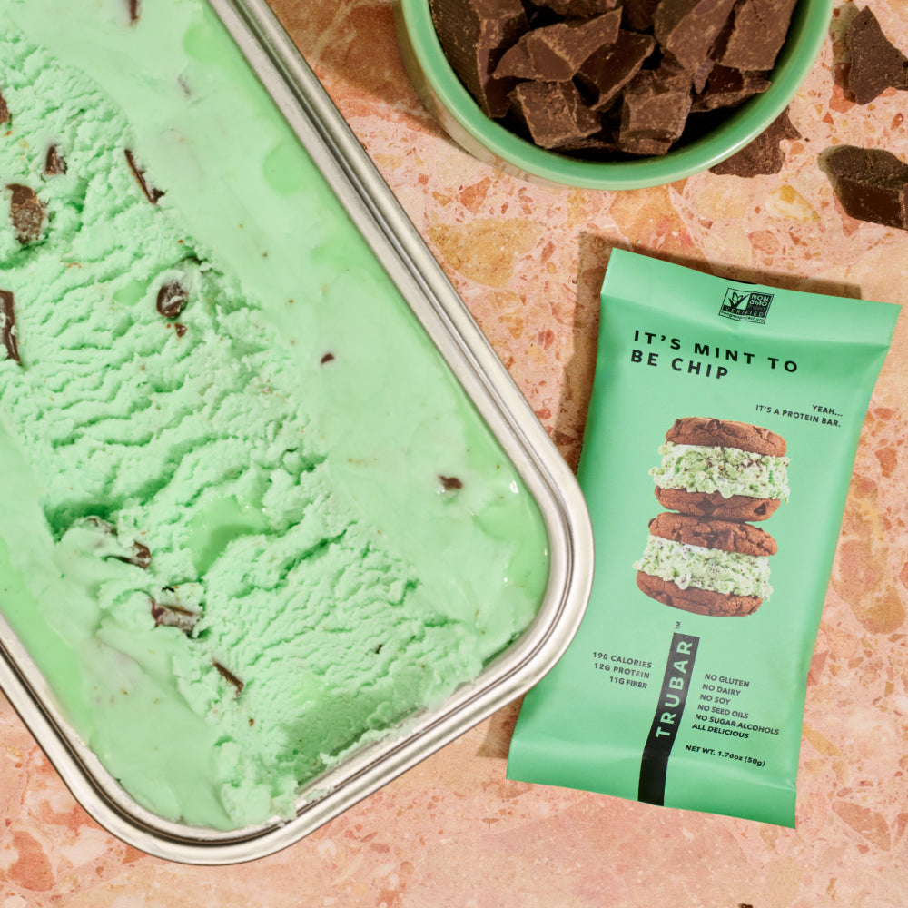 Mint green mint-chocolate protein bar beside green powder and chocolate pieces