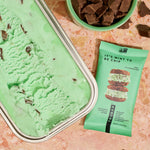 Mint green mint-chocolate protein bar beside green powder and chocolate pieces