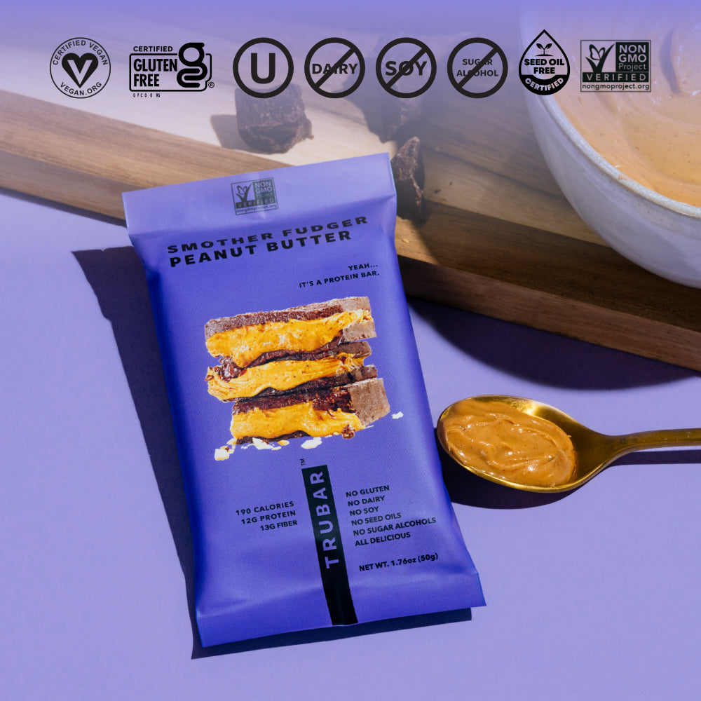 Purple protein bar pouch beside a spoon of peanut butter on a wooden surface