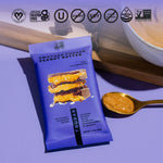 Purple protein bar pouch beside a spoon of peanut butter on a wooden surface