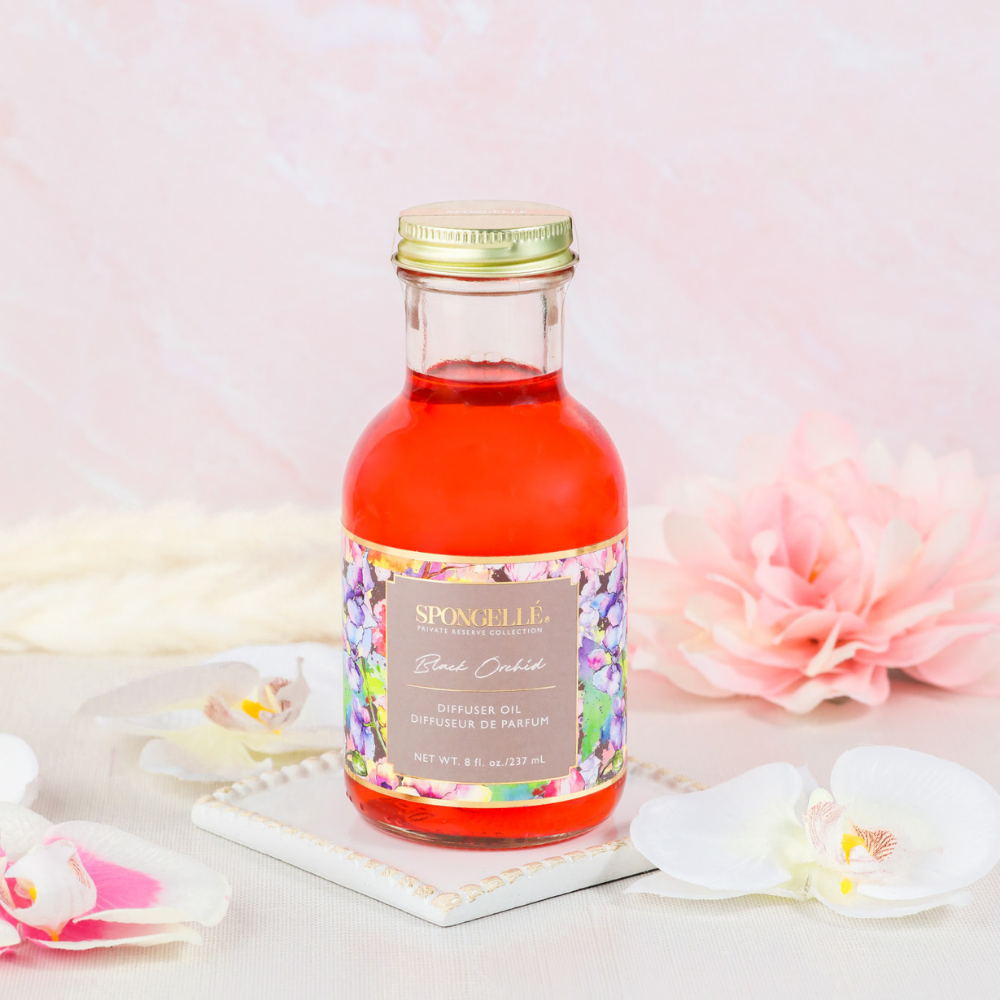Diffuser oil bottle with floral label, gold lid, and orange liquid in clear glass