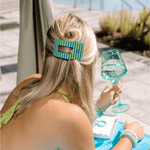 Teal and blue striped flat rectangle hair clip holding blond hair