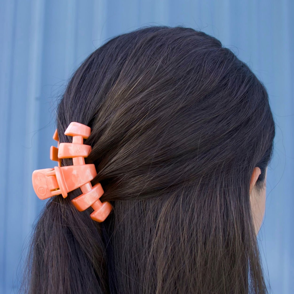 Small coral-orange claw clip on dark hair, securing the side section.