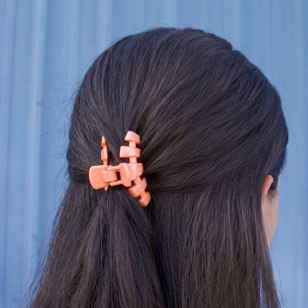 Coral-orange tiny claw clip holding dark hair in place