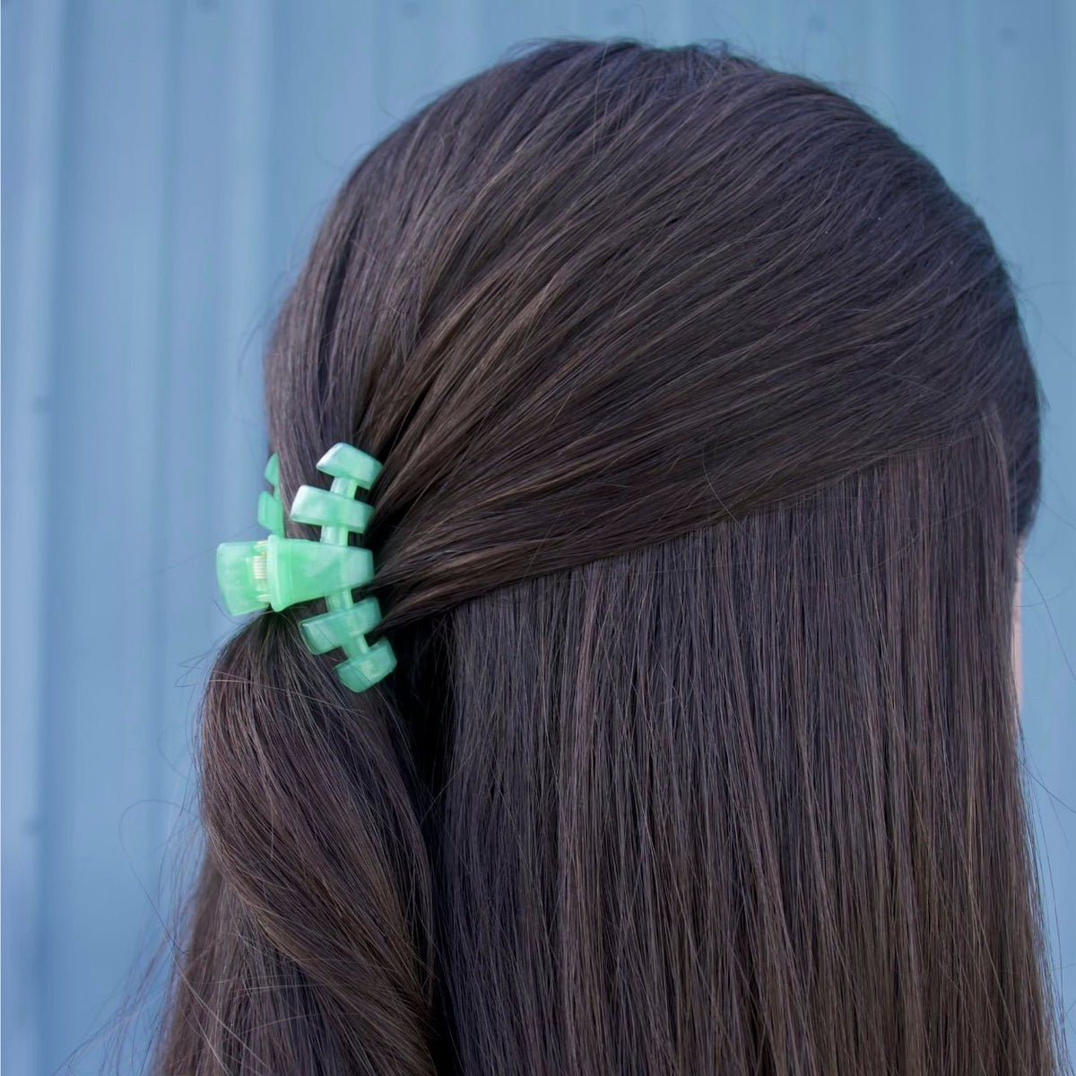 Small mint green claw clip holding dark hair to one side
