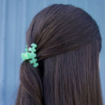 Small mint green claw clip holding dark hair to one side