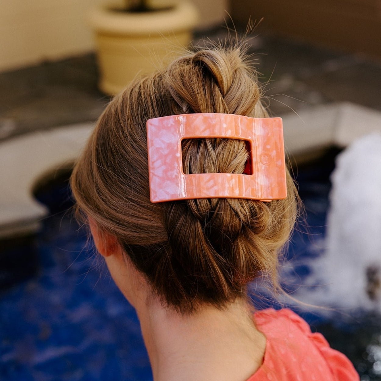 Coral-pink flat rectangle hair clip holding a low bun