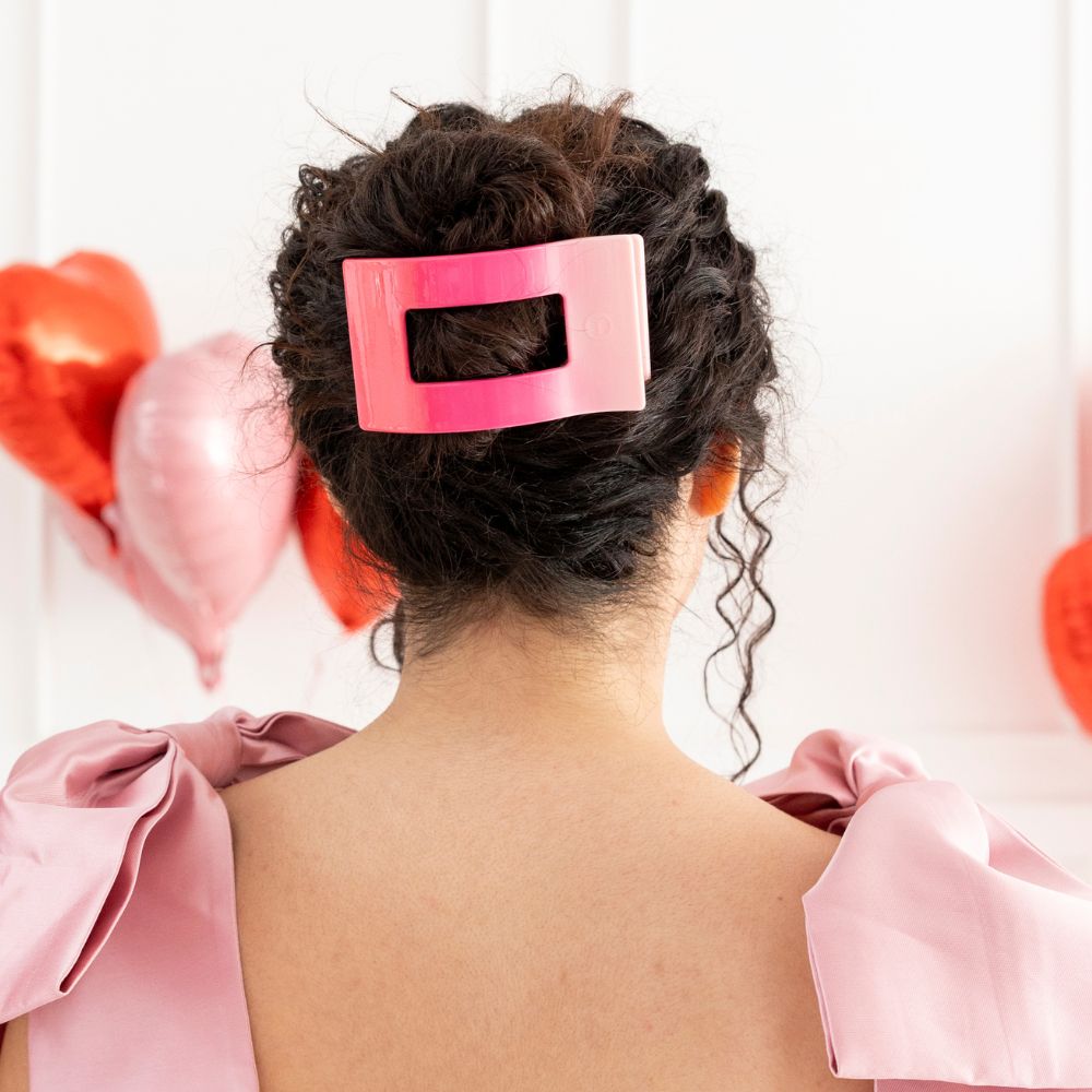 Pink flat rectangle hair clip securing curly updo; clip centered on back of head