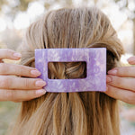 Lavender rectangular flat hair clip with marbled pattern held in blonde hair