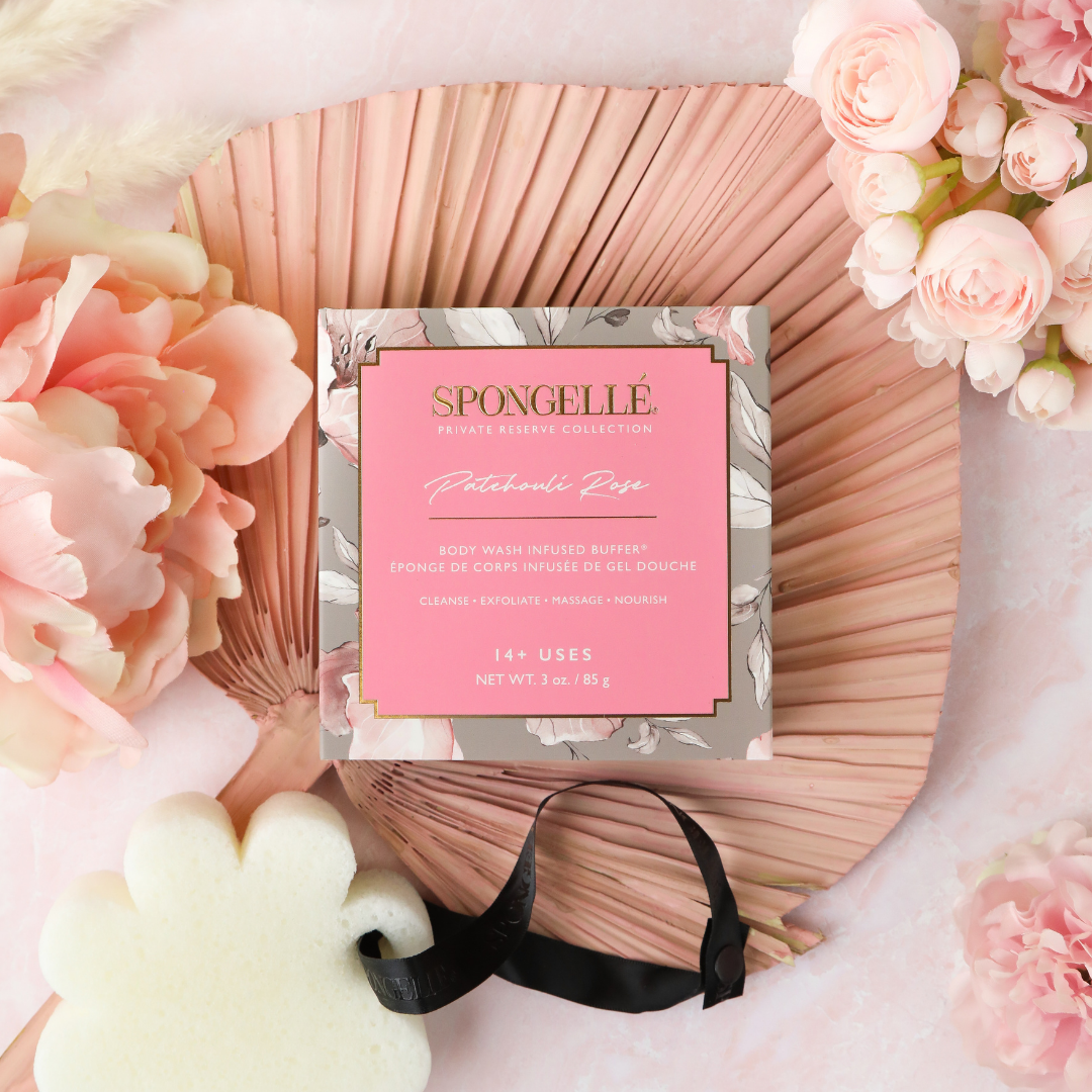 Flower-shaped body buffer with white sponge and black ribbon beside boxed soap