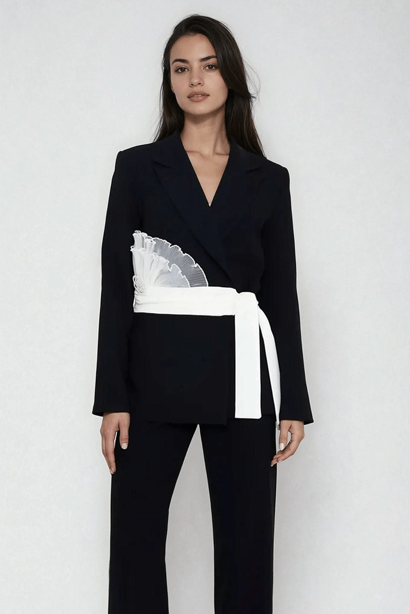Dark blazer with V-neck and white rosette belt detail at waist over matching pants