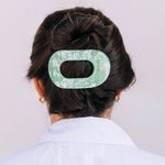 Large flat round hair clip in translucent mint green, securing dark hair in a bun