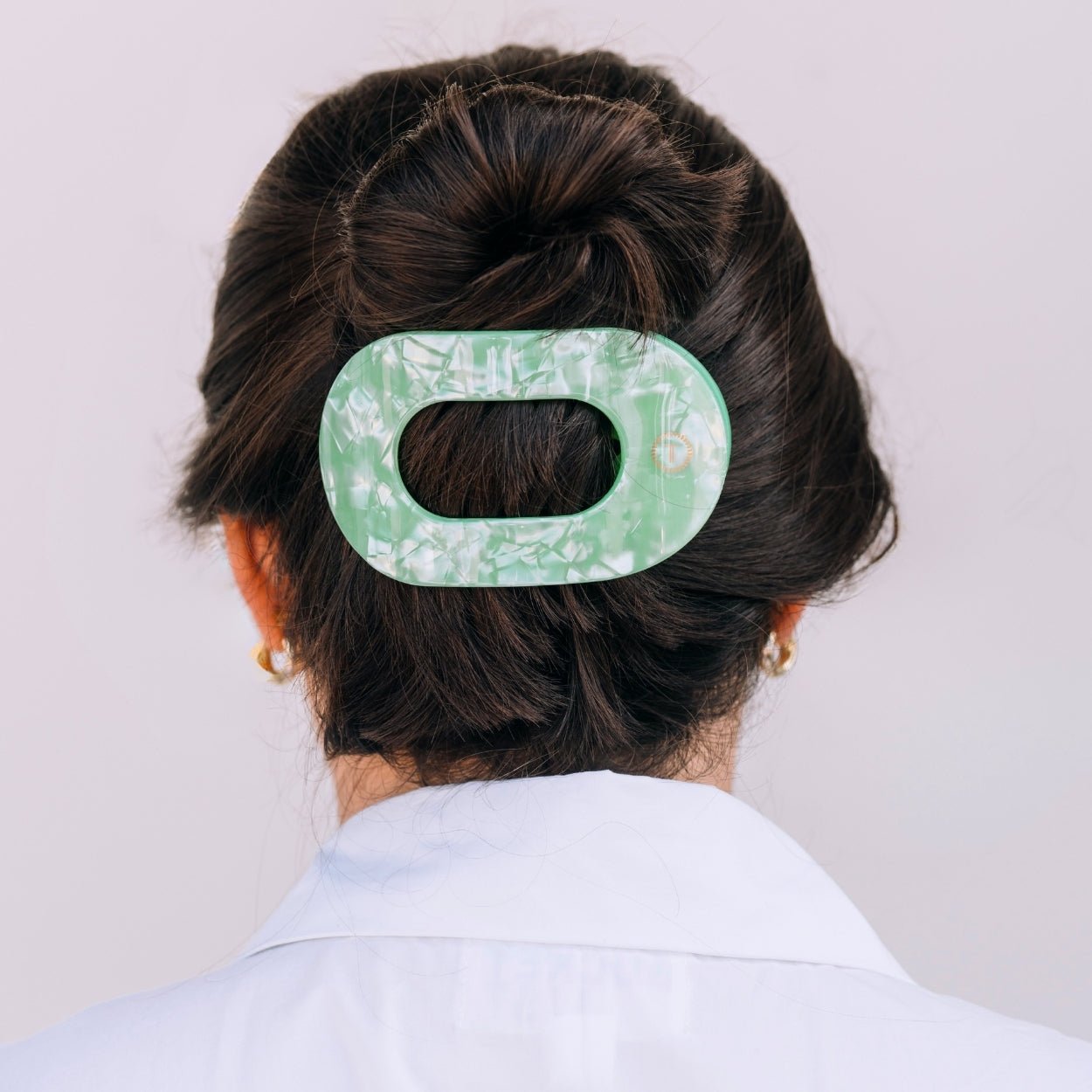 Large flat round hair clip in translucent mint green, securing dark hair in a bun