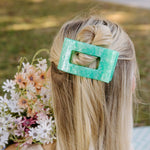 Mint green rectangular hair clip holding blonde hair.