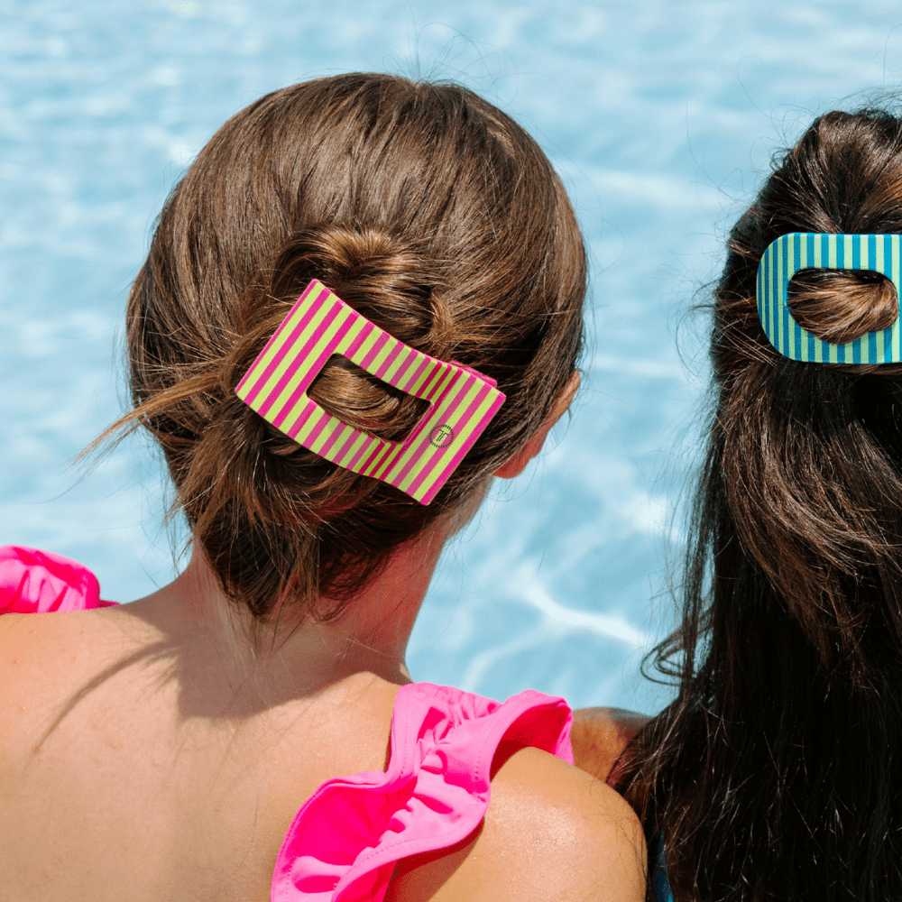 Large striped rectangle hair clip holding two hair sections, pink and green stripes.