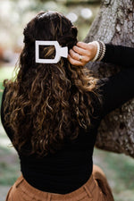Small flat square hair clip securing dark wavy hair on the side, cream finish
