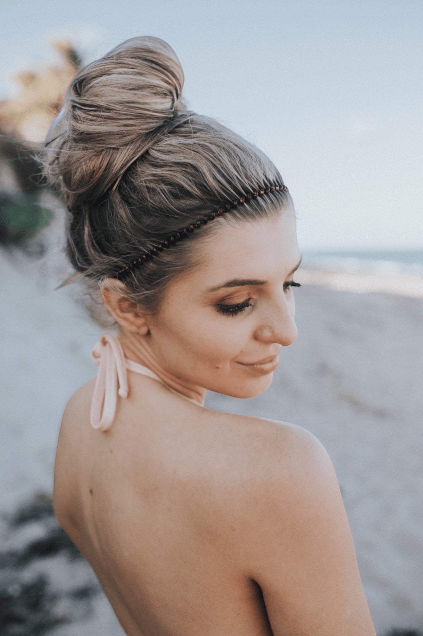 Beaded headband worn in a low bun with a round white T charm at the back