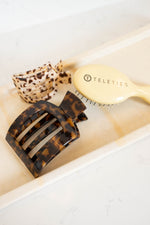 Flat square tortoise-pattern hair clip resting on white tray