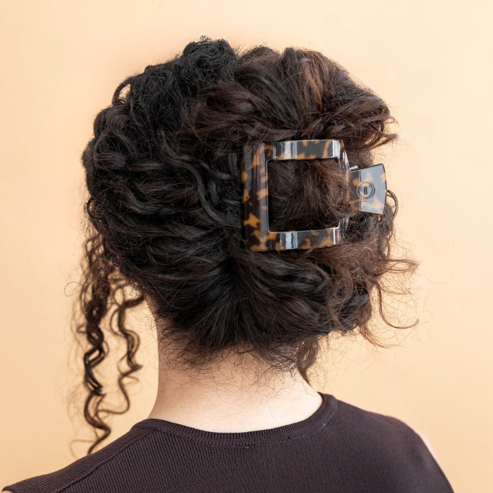 Tortoise-pattern flat square hair clip holding dark curly hair