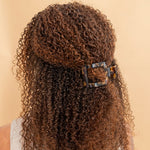 Tortoiseshell square hair clip holding curly hair back, flat design