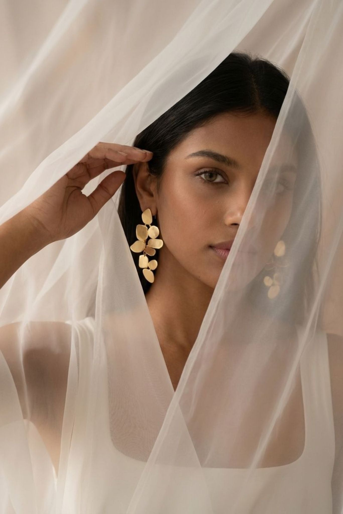 Gold-toned floral dangle earrings on a model behind a sheer veil