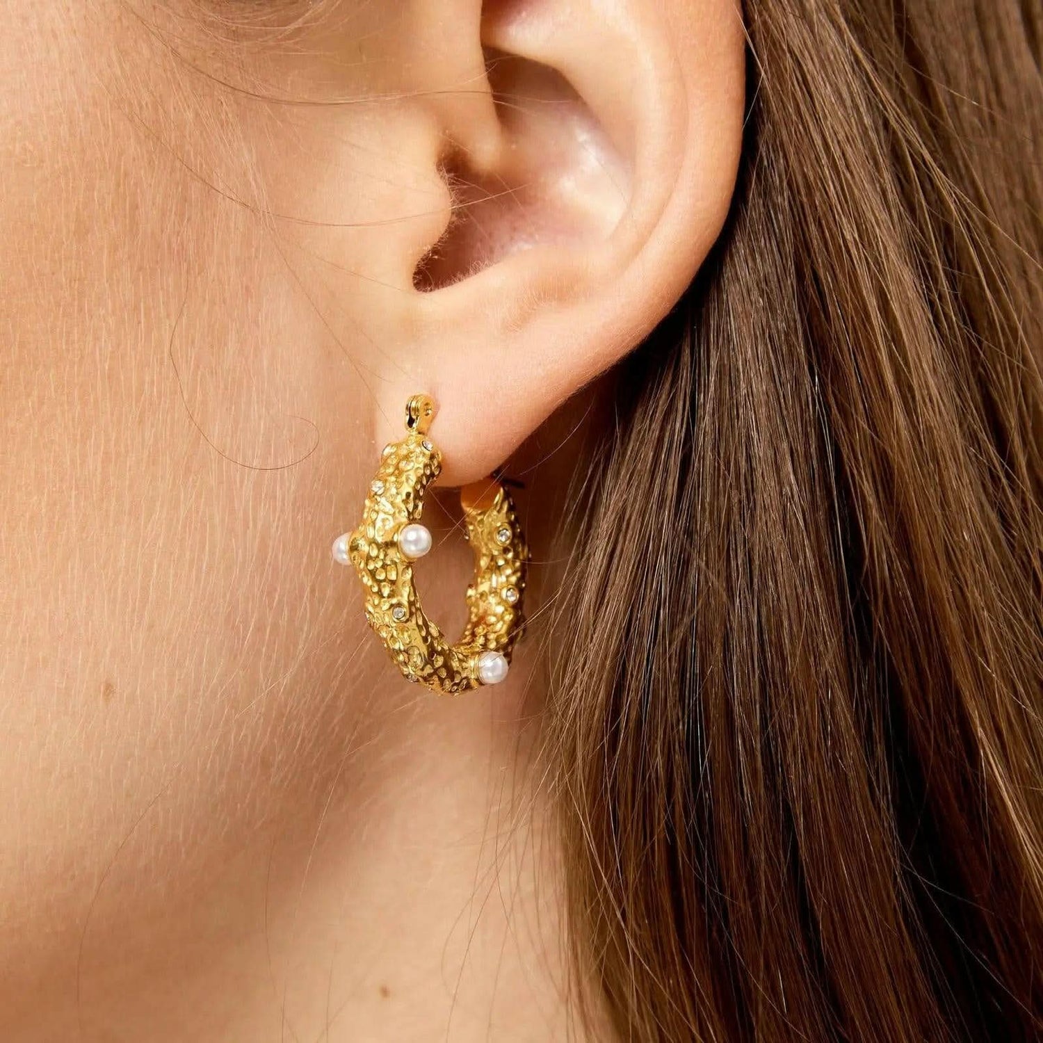 Gold hoop earrings with white pearl beads, worn on an ear close-up